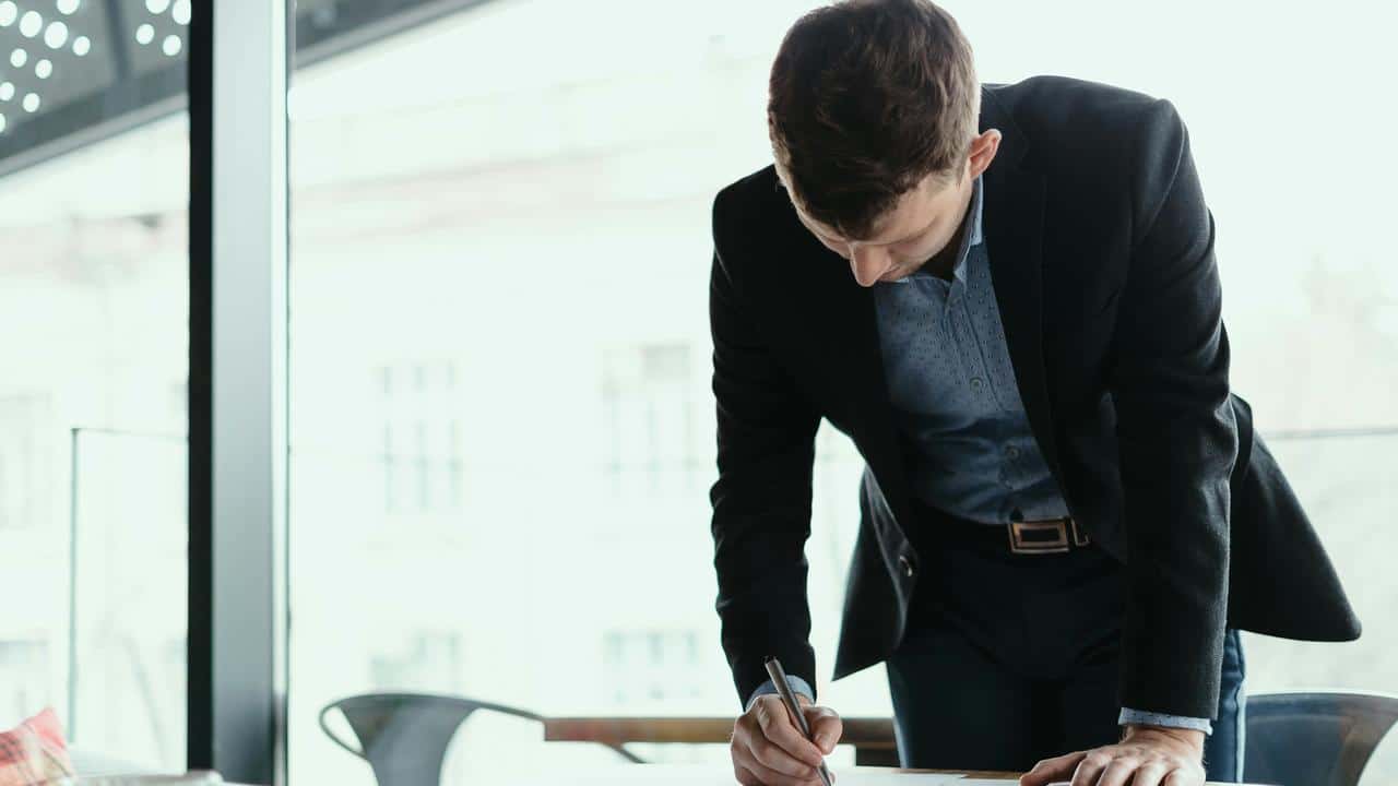 A person in a suit writing on a document.