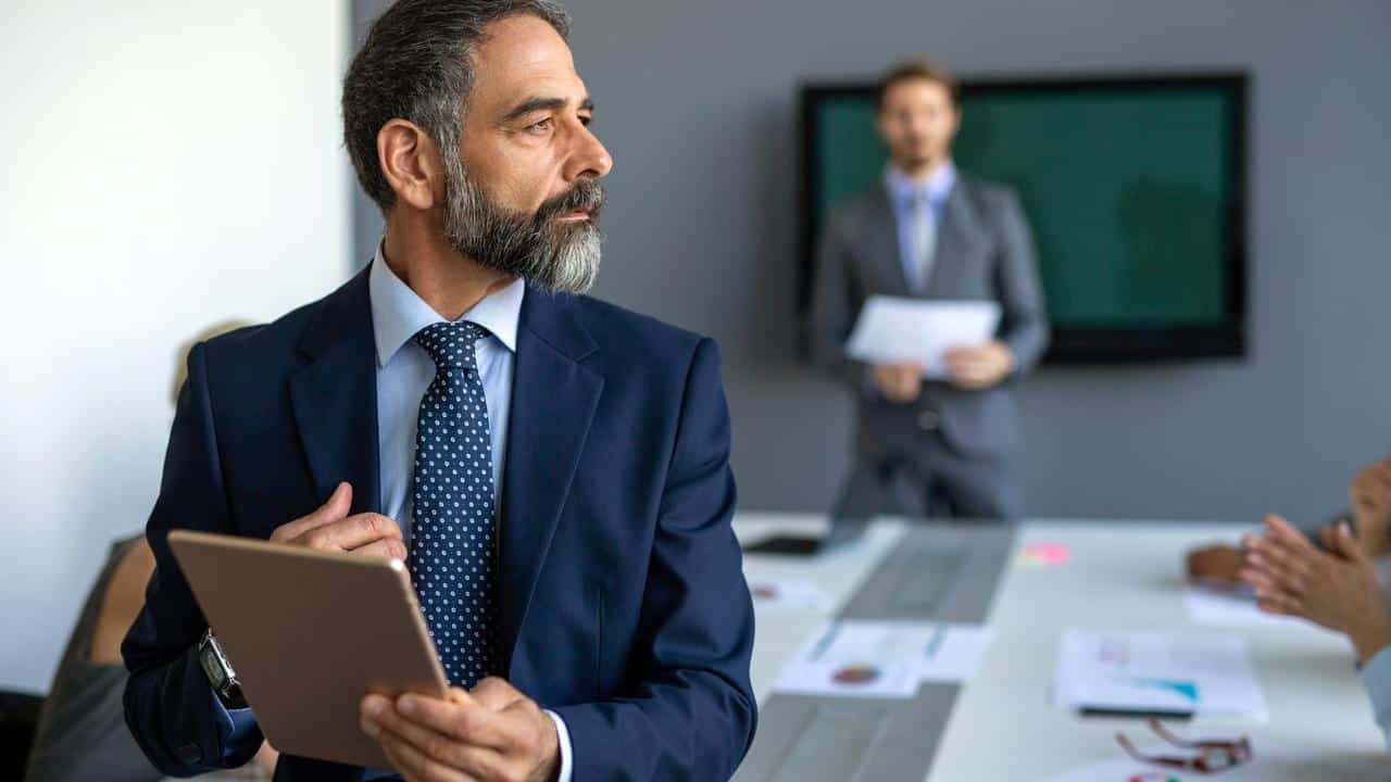 A man in a suit holding a tablet in a meeting.