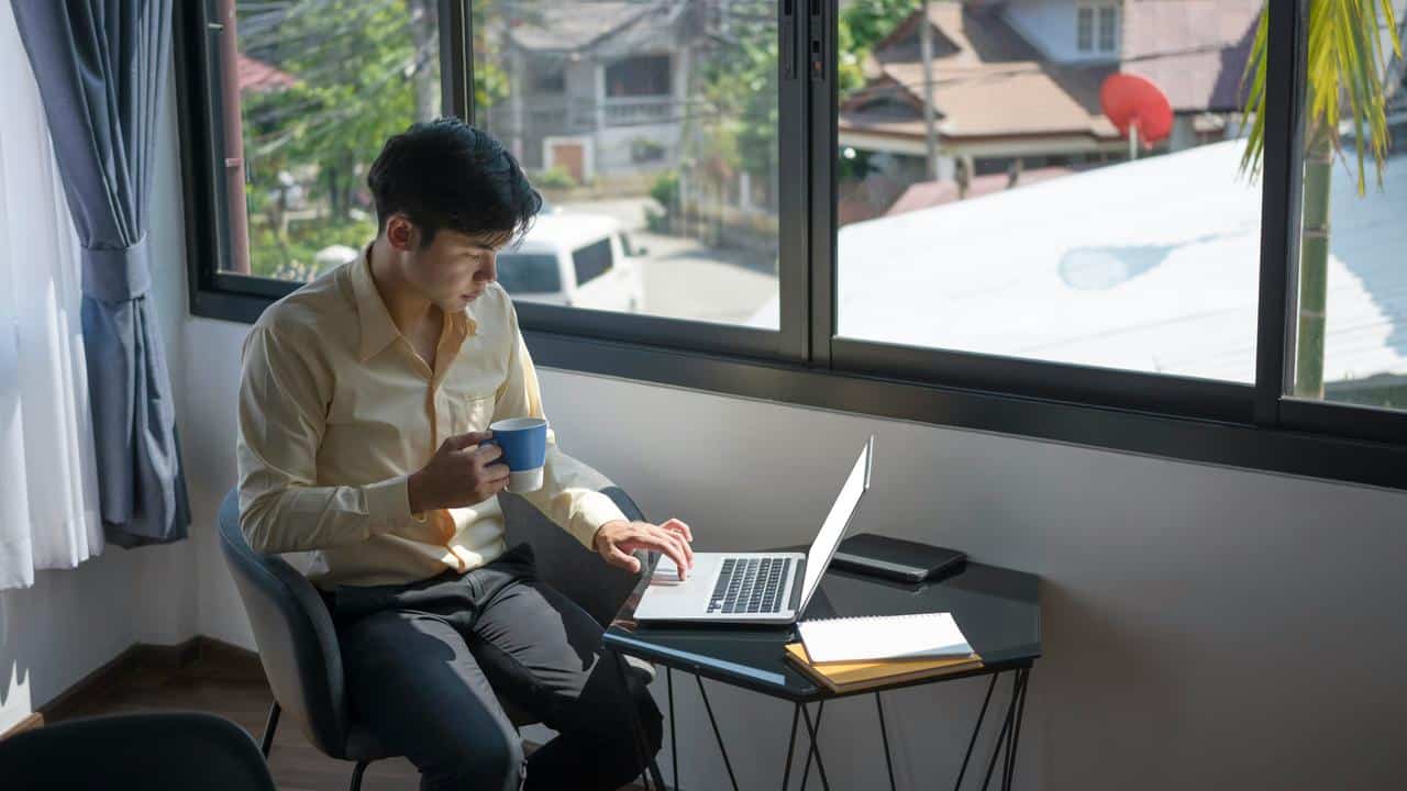 A man working on a laptop while holding a coffee mug.