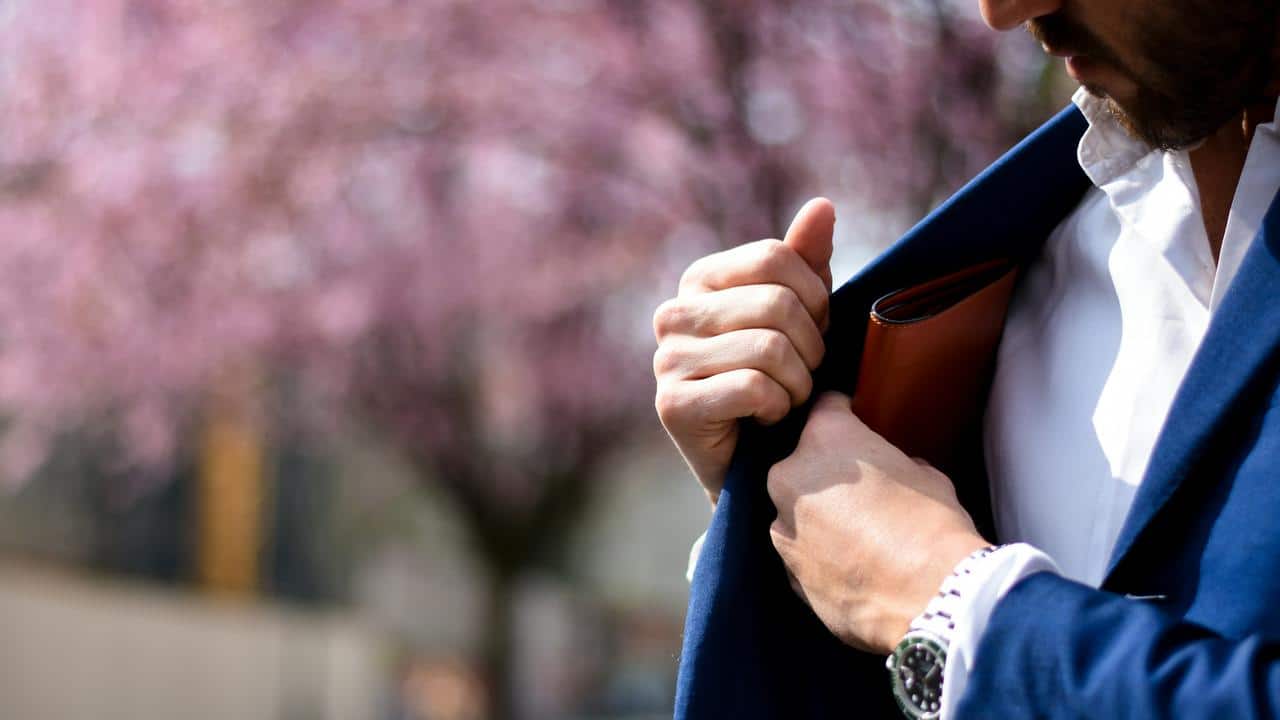 A person's hand putting a wallet into a suit pocket.