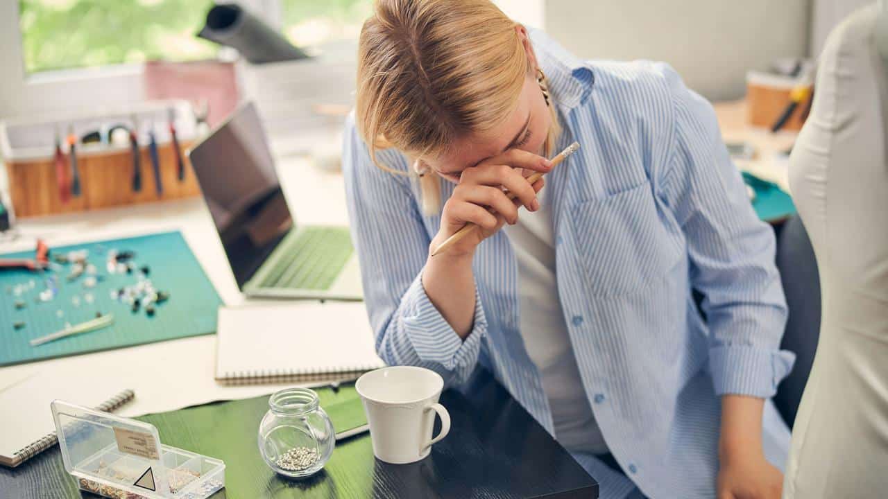 A person sitting at a desk looking stressed with a hand on their face.