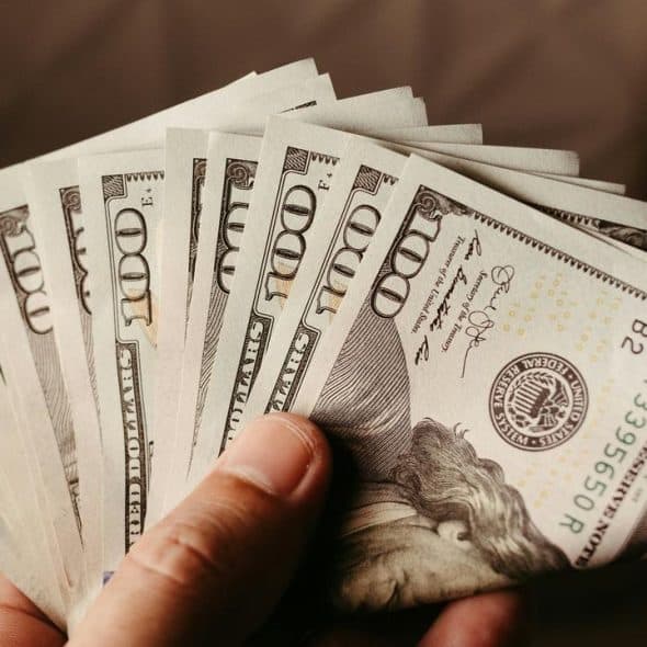A person's hand holding a fan of hundred-dollar bills.