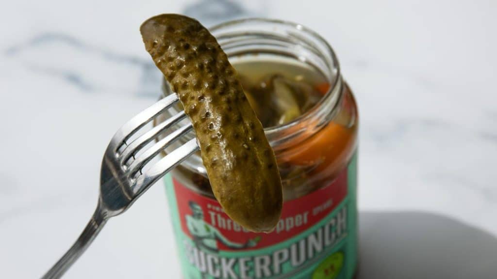 A pickle held over a jar with a fork.