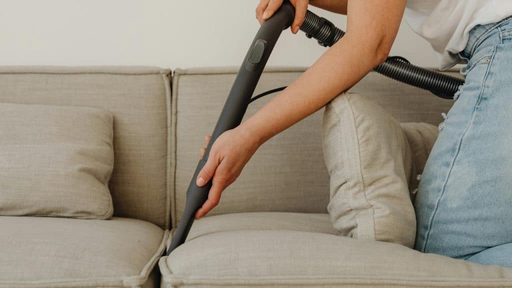 A person vacuuming a beige sofa.