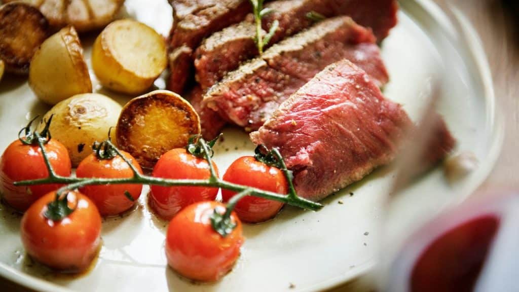 A plate of rare steak with potatoes and cherry tomatoes.