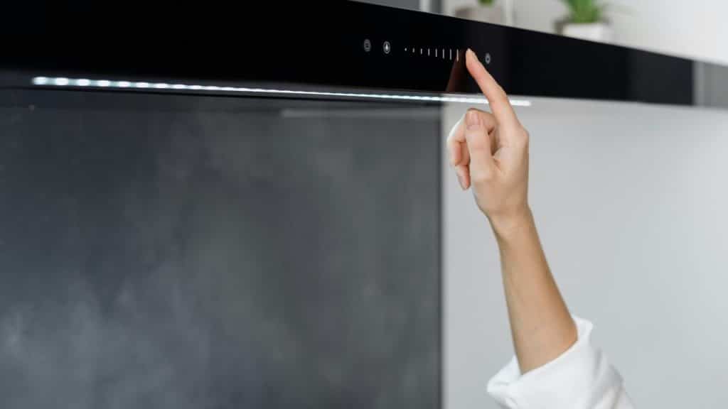 A person’s hand adjusting the digital controls of a kitchen range hood.