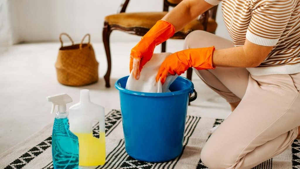 A person wearing gloves cleaning with a bucket and sprays.