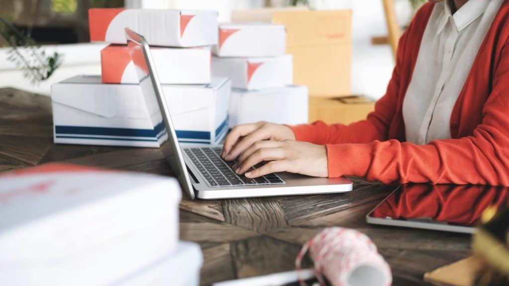 An individual typing on a laptop surrounded by shipping boxes.