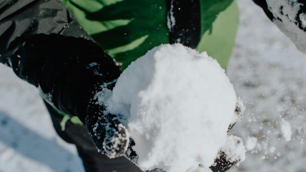 A person holding a large snowball in gloved hands.