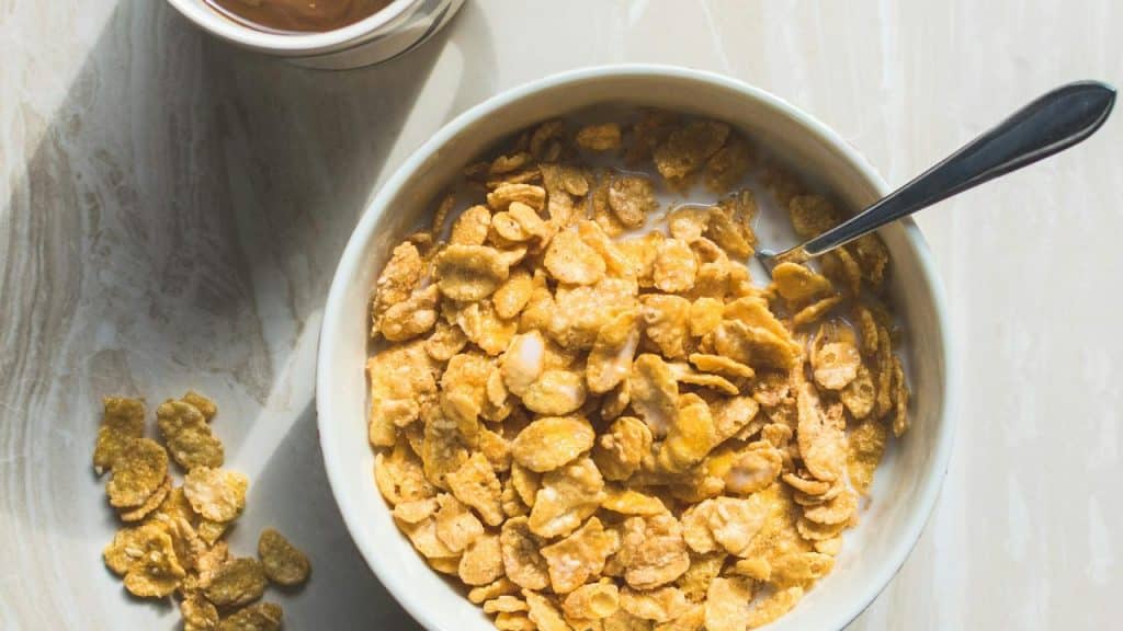 A bowl of cornflakes with milk and a spoon.