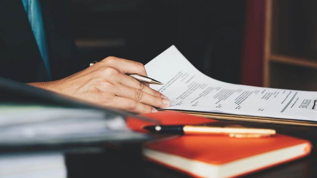 A person reviewing a printed resume with a pen in hand.