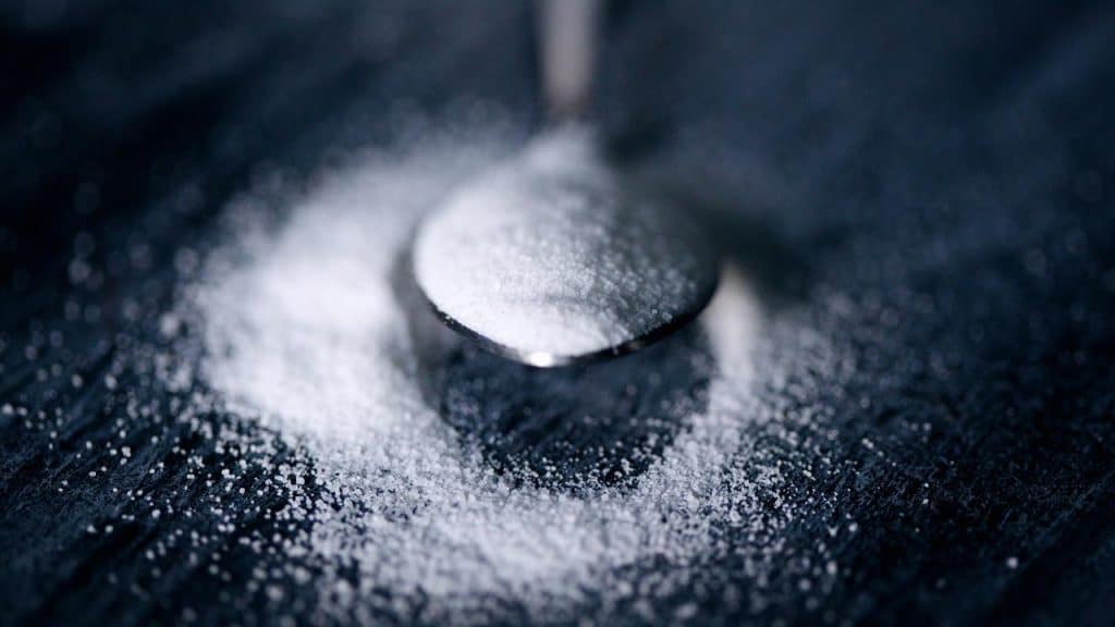 A spoonful of granulated sugar on a dark surface.