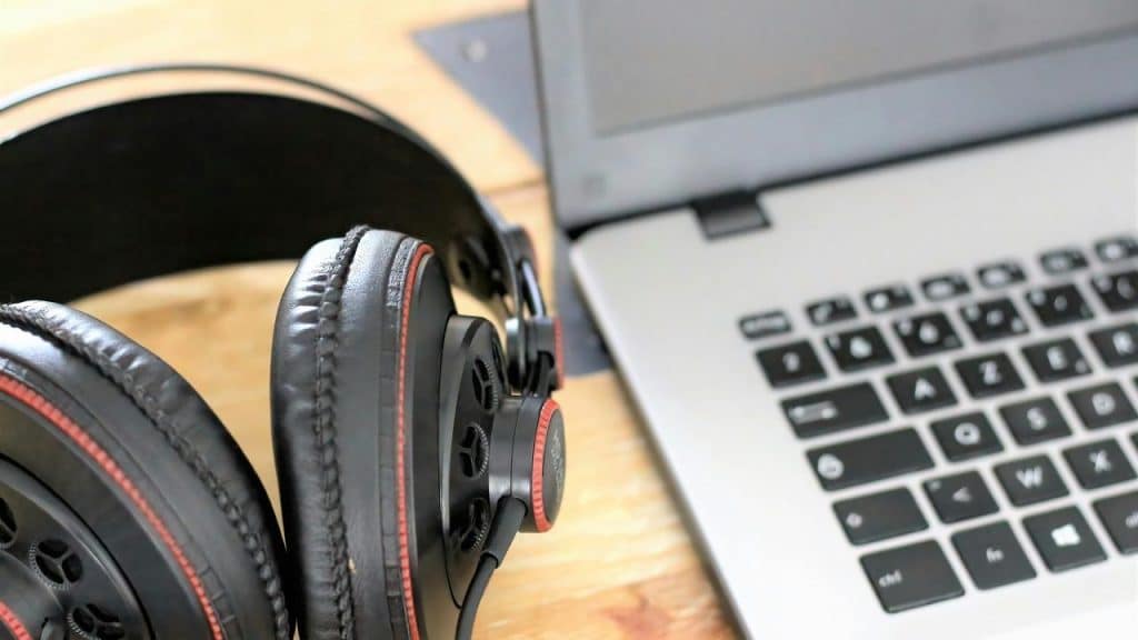 A pair of black headphones next to a laptop on a wooden desk.