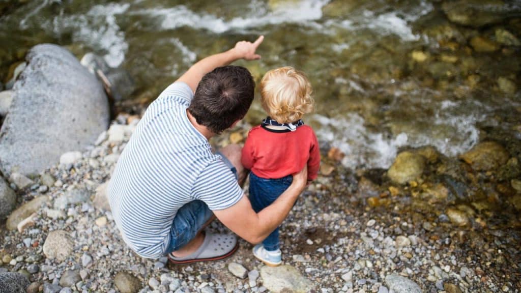 A father and his child looking at a flowing river.