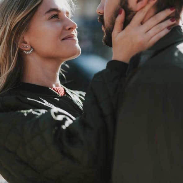 A woman gazing lovingly at a man while holding his face outdoors.