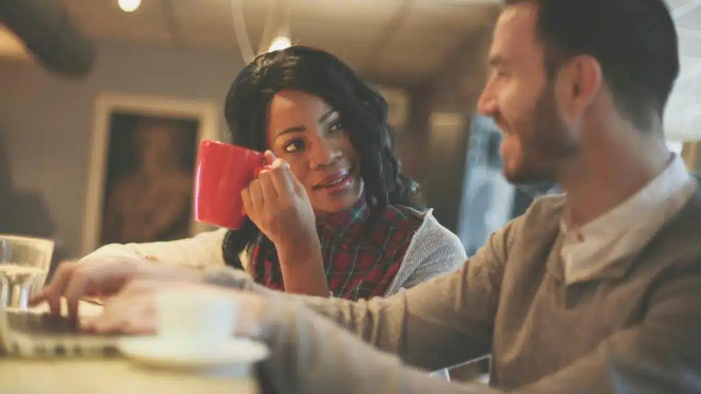 A woman holding a red mug while talking to a man.