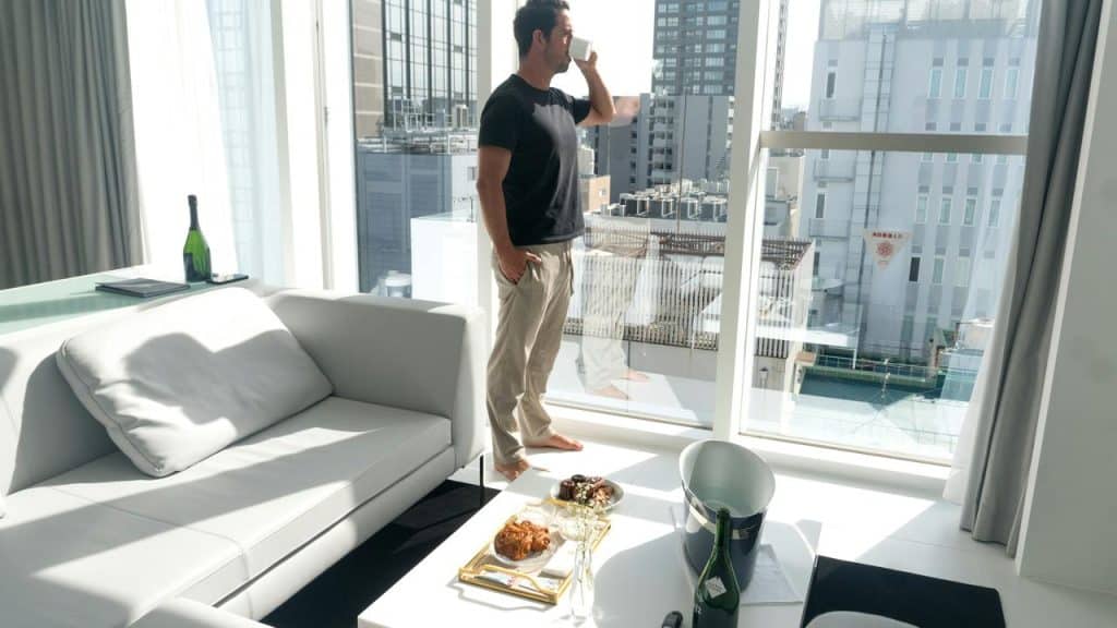A man drinking coffee by a window in a modern apartment.