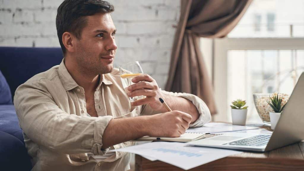 A man drinking lemon water while working at a laptop.