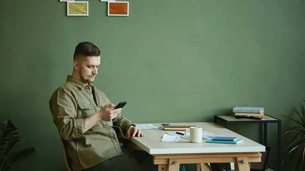 A man sitting at a desk looking at his phone.