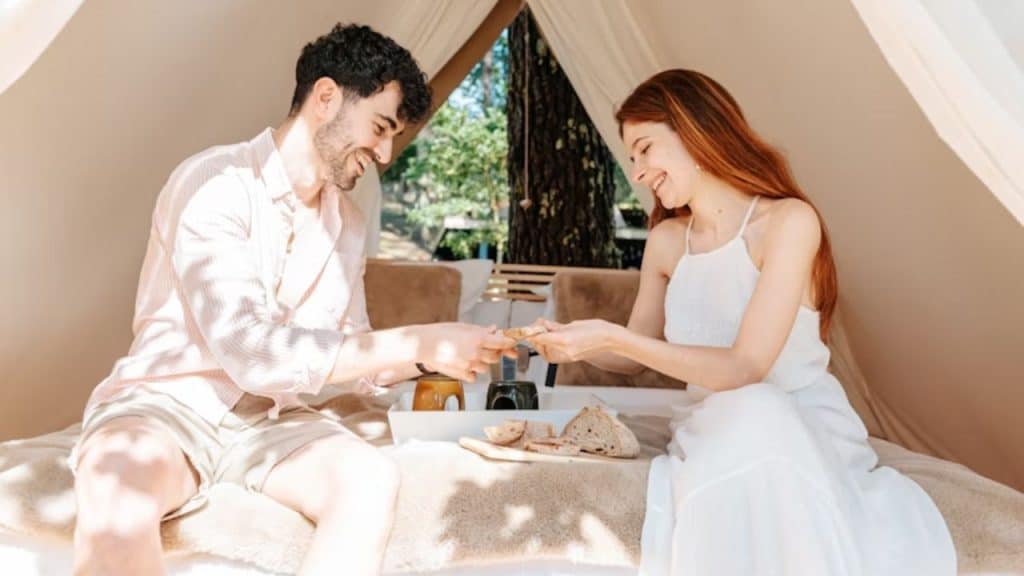 A couple in an elegant glamping tent lit among forest trees.