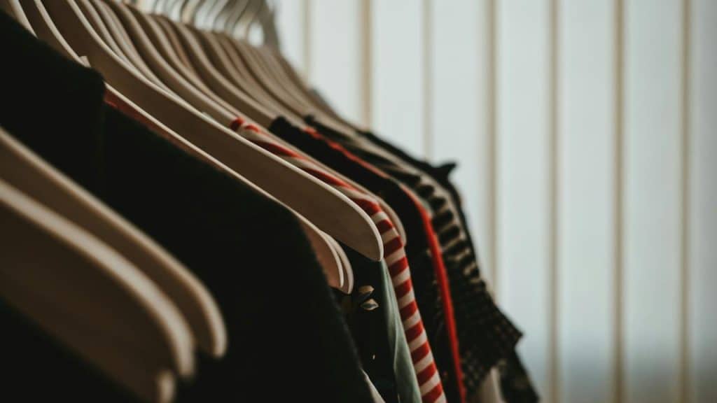 A row of clothes hanging on wooden hangers in a closet.