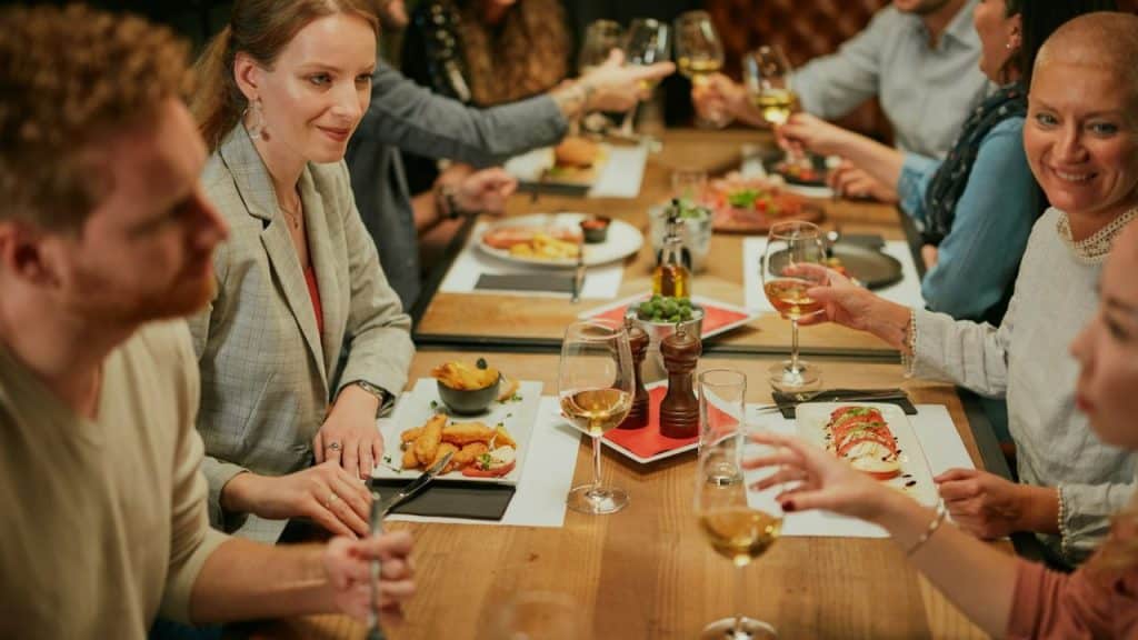 A diverse group of friends clinks glasses and eats dinner together at a restaurant.