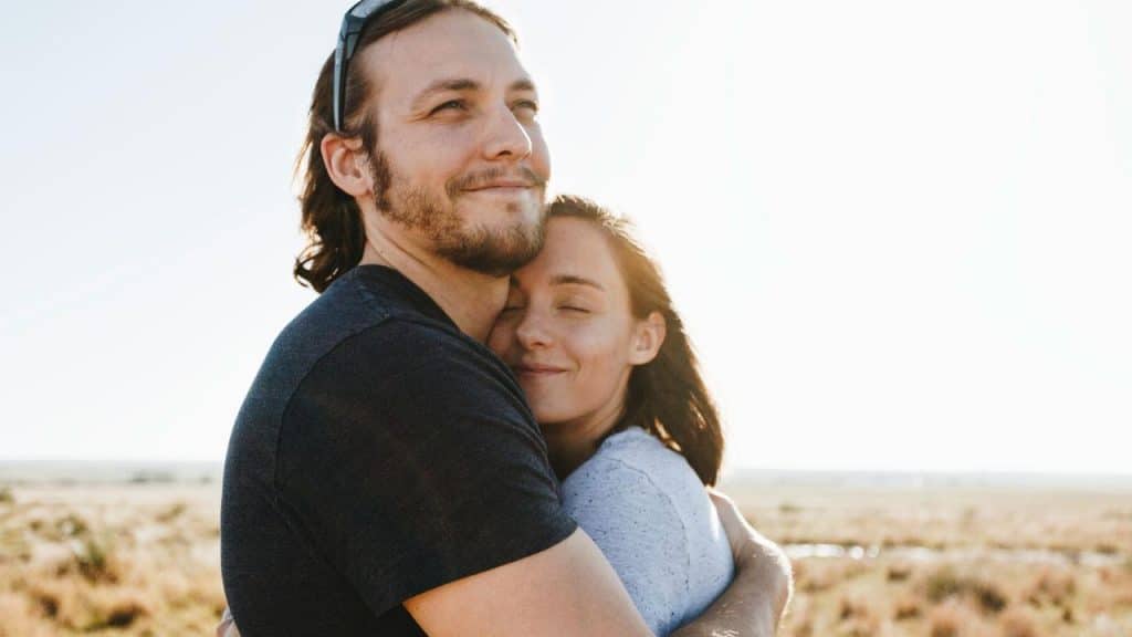 A happy couple hugging in a sunlit open field.
