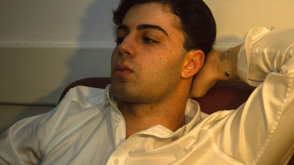 A pensive man in a white shirt is holding the back of his neck.