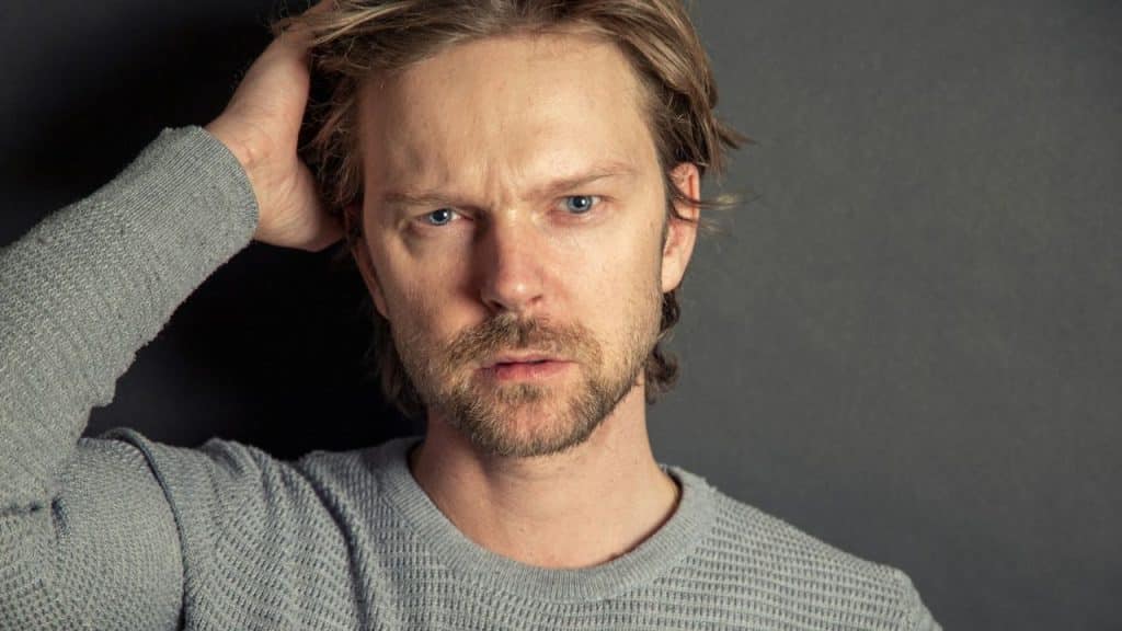 A serious man with a beard and mustache is holding his head.