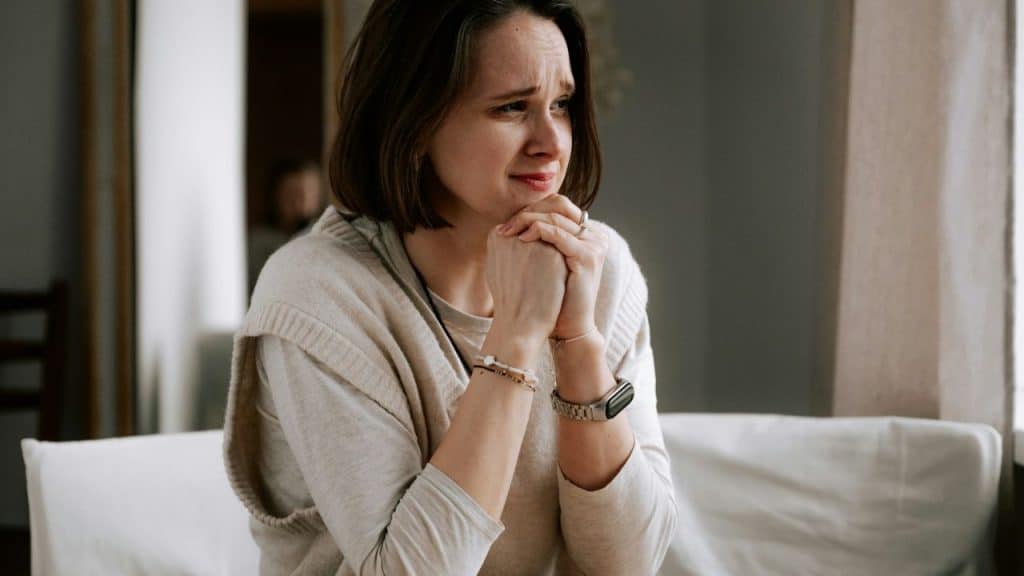 A concerned woman is sitting with her hands clasped under her chin.