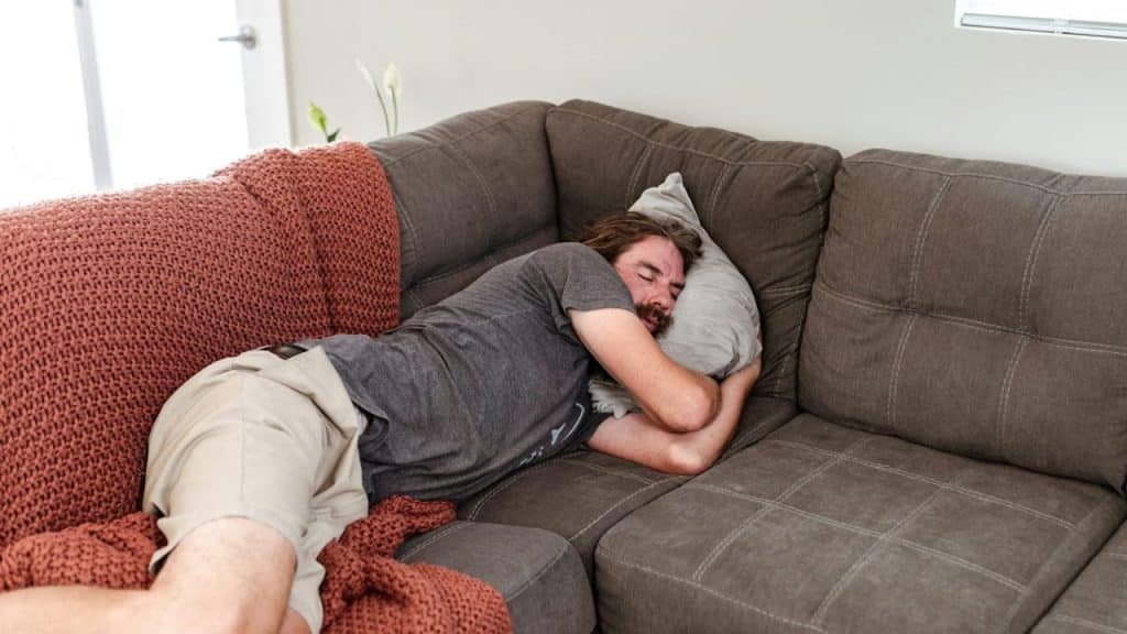 A man is sleeping on a couch with a pillow over his head.