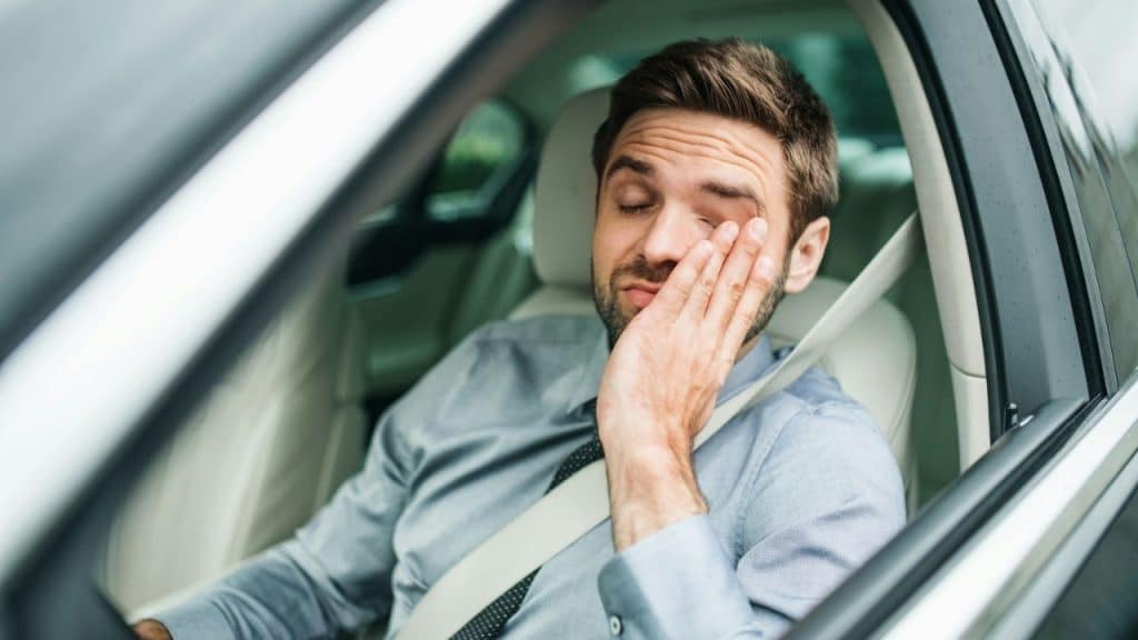 A weary man is sitting in a car and rubbing his eye.