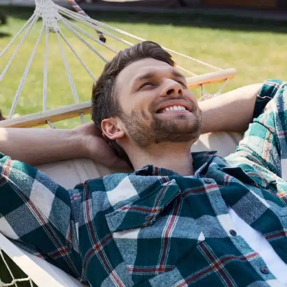 A man relaxing in a hammock outdoors, smiling.