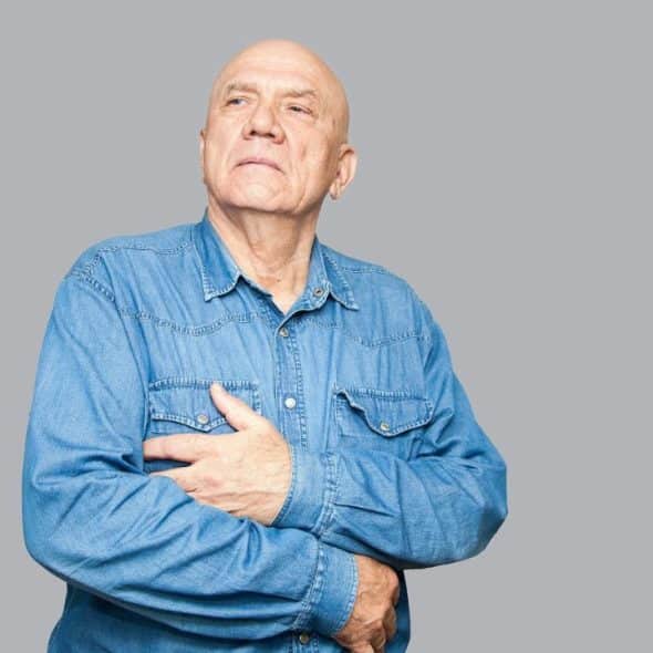 A thoughtful, bald, elderly man is holding his stomach.