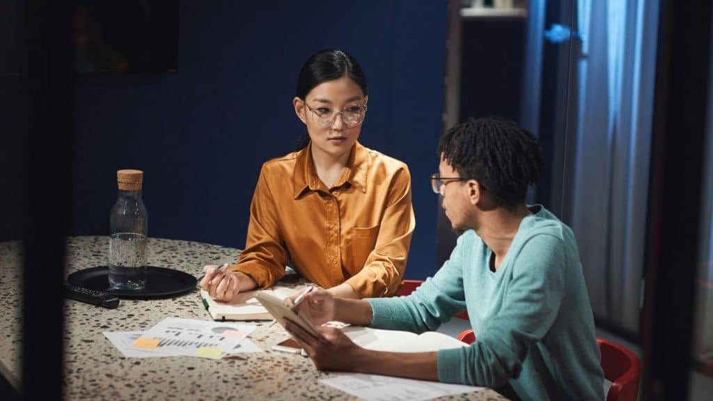A couple sitting at a table with papers, appearing to discuss something seriously in a professional or transactional manner.