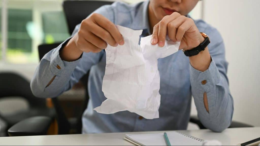 A person tearing a piece of paper at a desk.