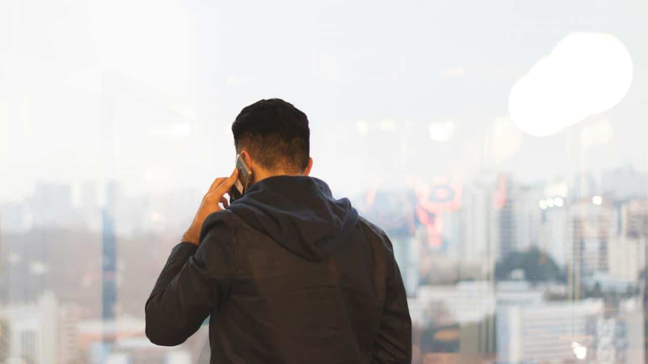 A man in a hoodie talking on a phone while facing a city view.
