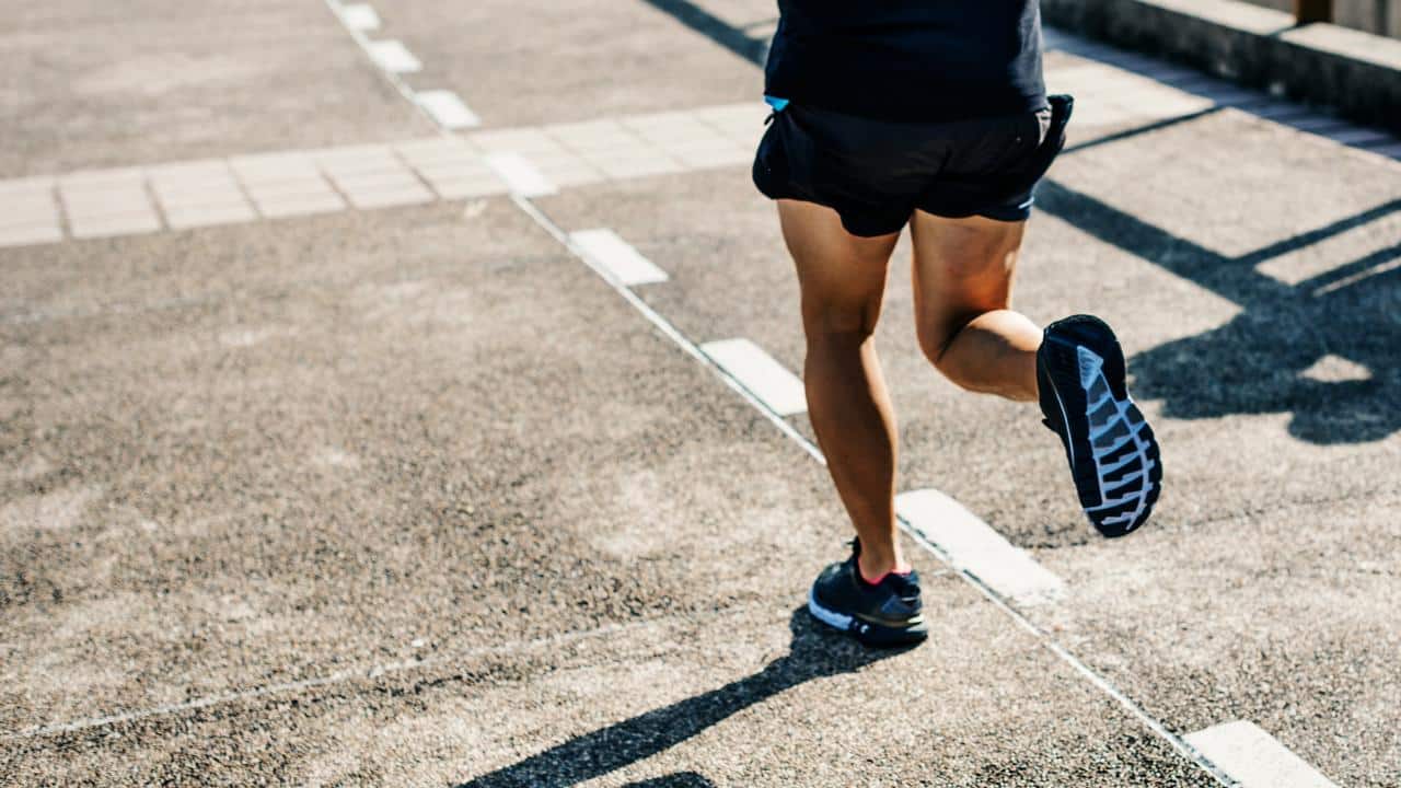 A person running on a paved path wearing black athletic shoes.