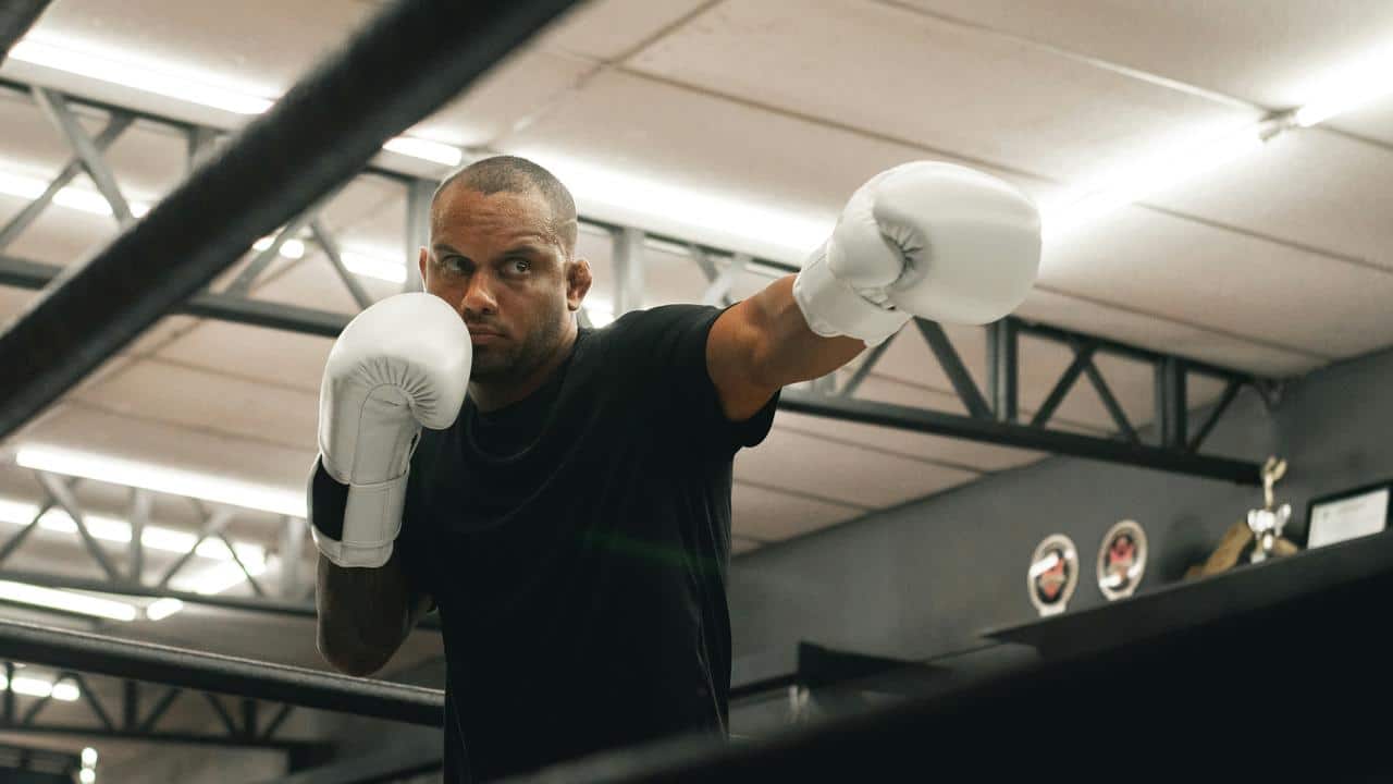 A man wearing white boxing gloves practicing in a gym ring.