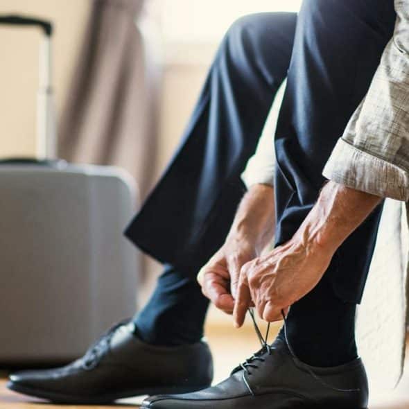 A person tying their shoes next to a suitcase.