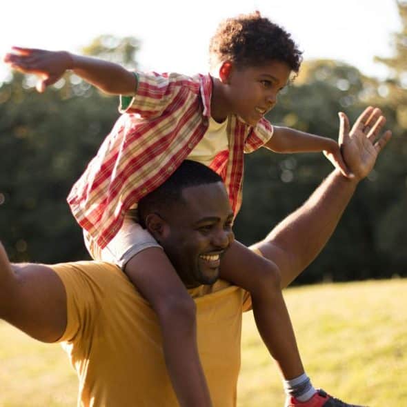 A father carrying his child on his shoulders outdoors.