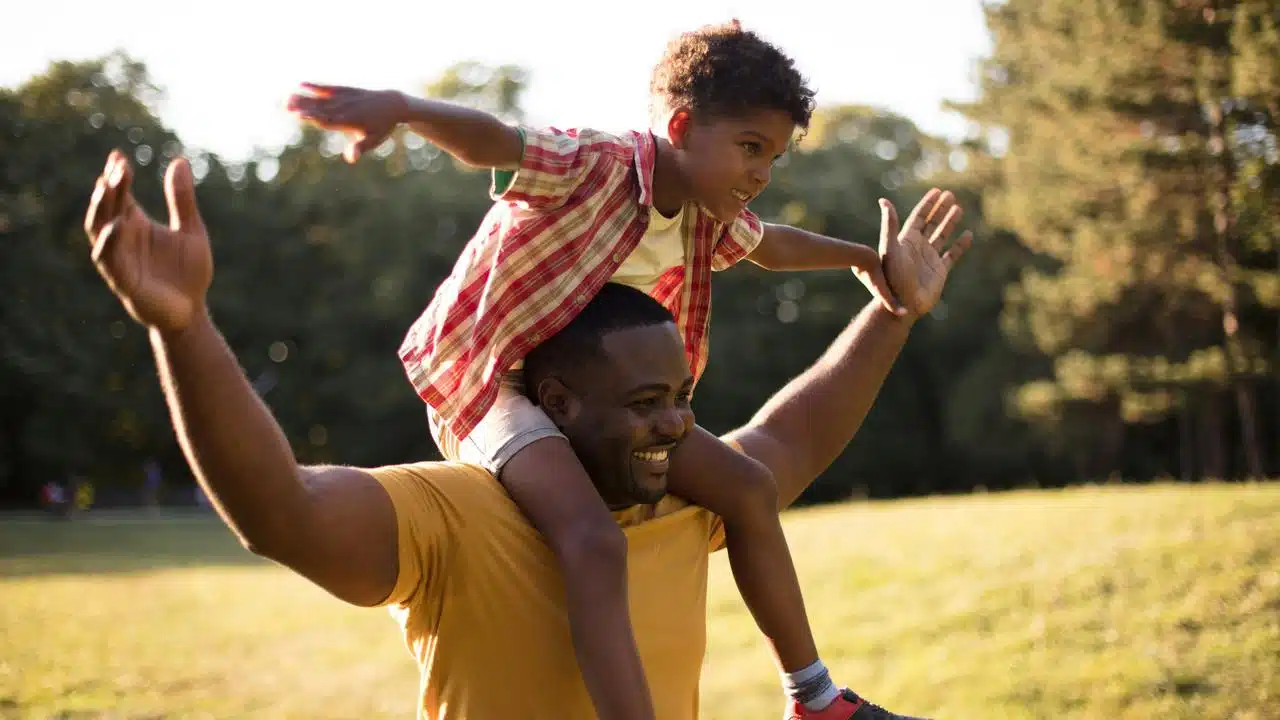 A father carrying his child on his shoulders outdoors.