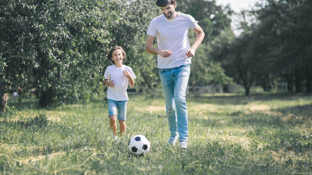 A father playing soccer with his child outdoors.