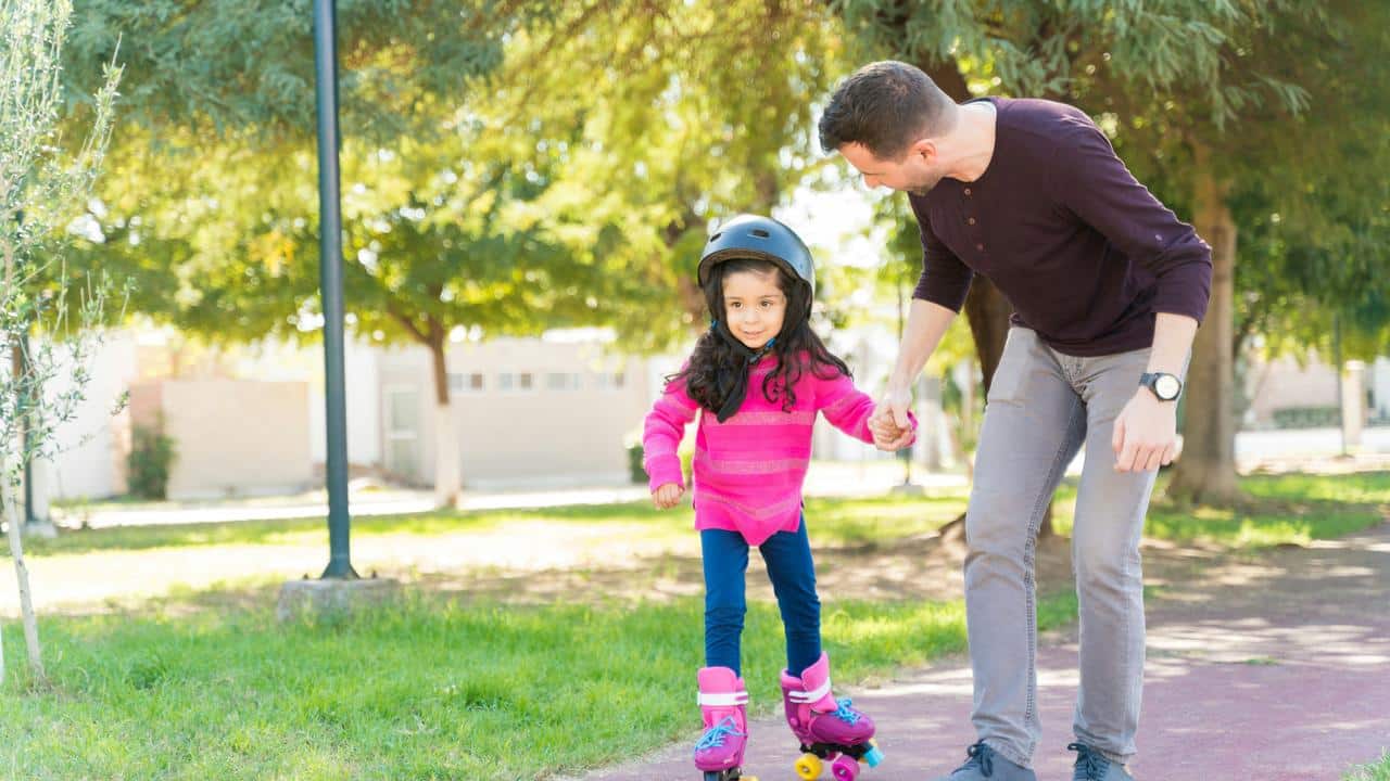 A father helping his daughter roller skate in the park.