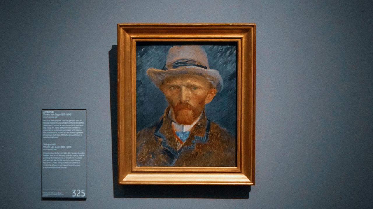 A framed self-portrait painting of Vincent van Gogh on a gray wall.