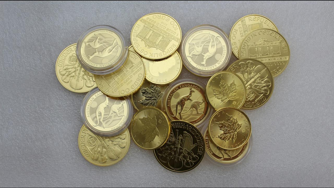 A collection of gold bullion coins on a gray surface.