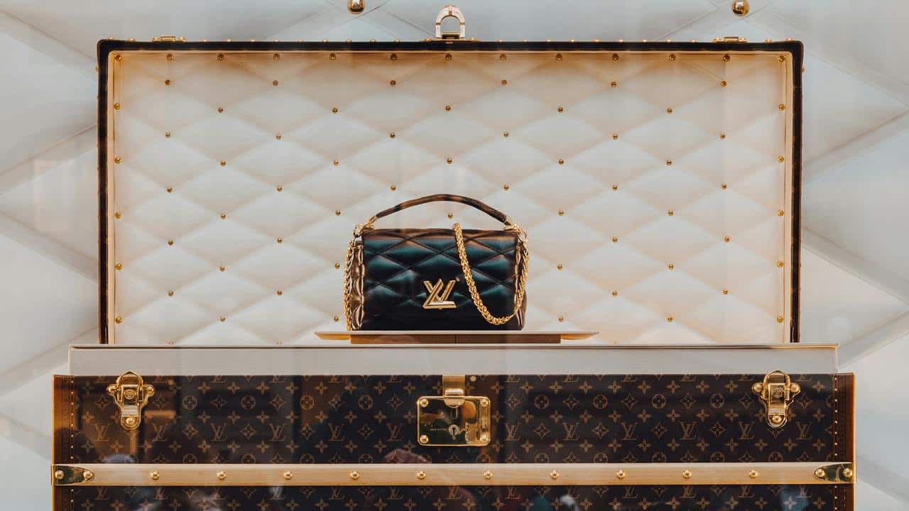 A black Louis Vuitton handbag with a gold chain in a luxury display case.