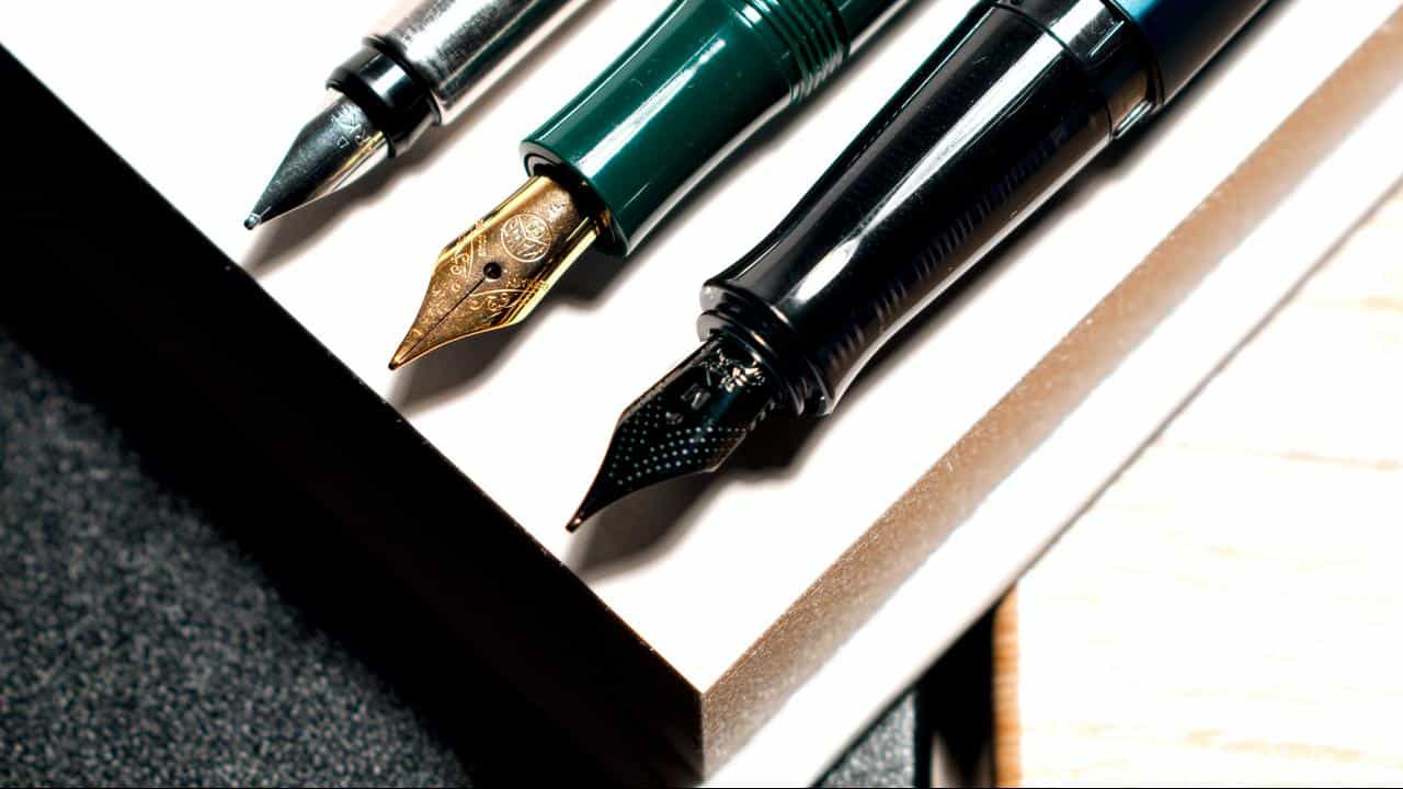A close-up of elegant fountain pens resting on a white notepad.