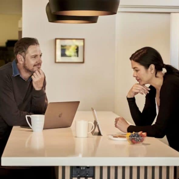 A couple sitting at home with a laptop and coffee mugs, smiling while checking their finances together.