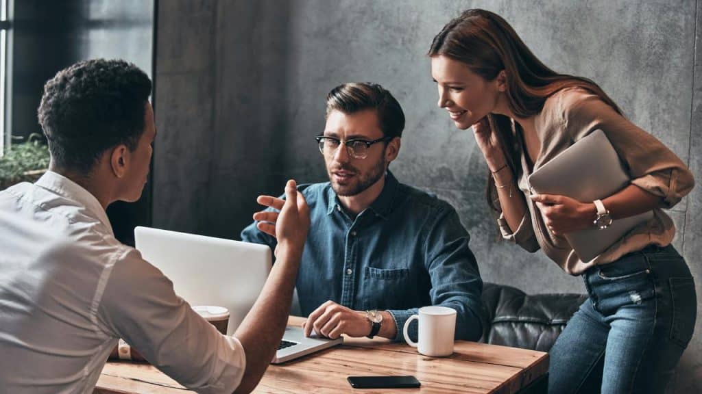 A group of three colleagues talking around a laptop.
